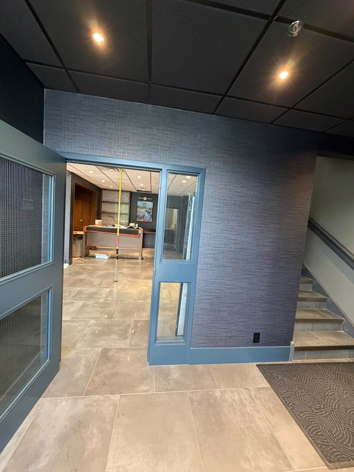 Charcoal woven-texture commercial wallcovering in a showroom reception lobby with stair, Highfield, SE Calgary