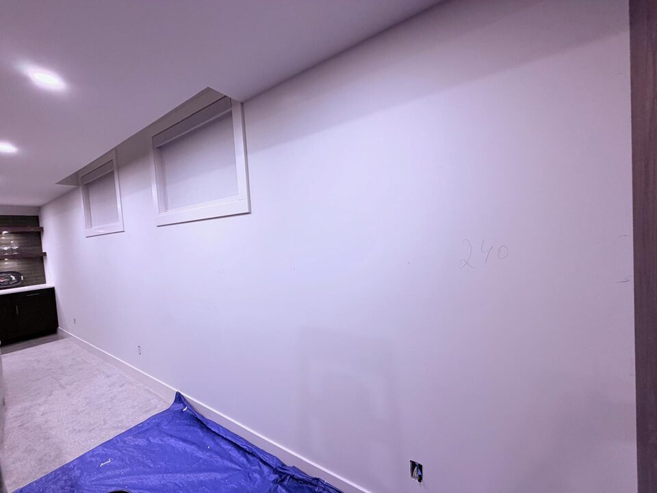 Primed basement wall with two windows in an Altadore, Calgary home before JF Fabrics Avalon wallpaper installation