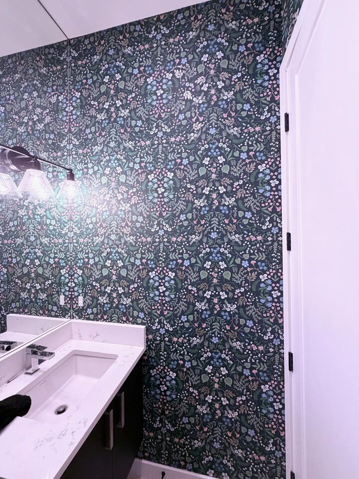 Dark green Wildwood floral wallpaper beside the vanity and mirror of a new-build powder room in Altadore, Calgary