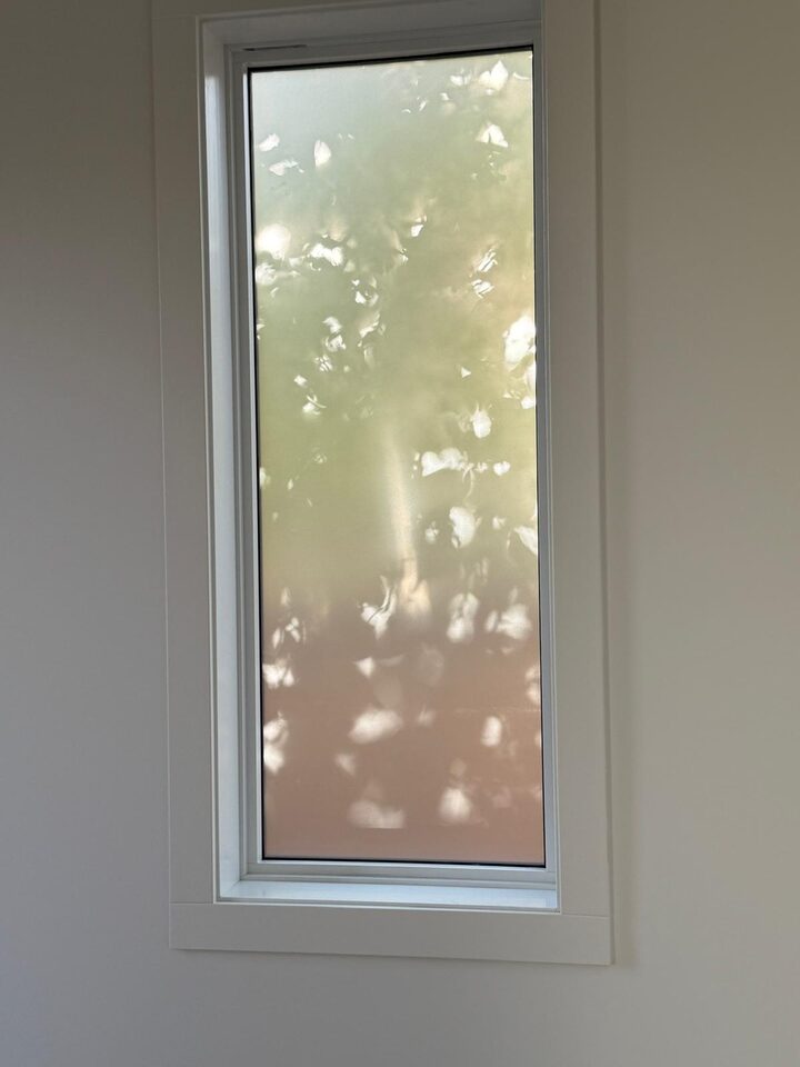 Dusted crystal frosted privacy film on a tall casement window in Bridgeland, Calgary, with leaf shadows softly showing through