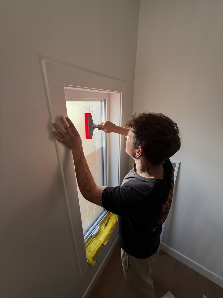 Wall Style Innovations installer squeegeeing dusted crystal frosted privacy film onto a tall casement window in a Bridgeland, Calgary new build
