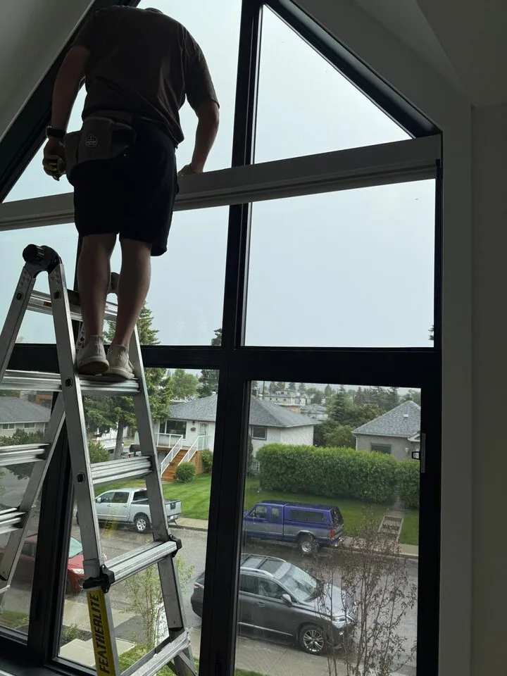 Solar window film being mounted and trimmed on a tall angled black-frame window during installation in Capitol Hill NW Calgary