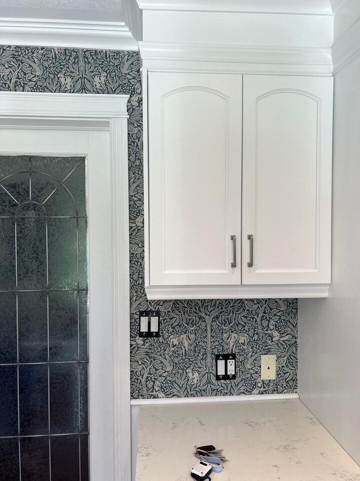 After photo of black and white botanical wallpaper installed behind cabinetry and door trim in a Deer Run SE Calgary dining room