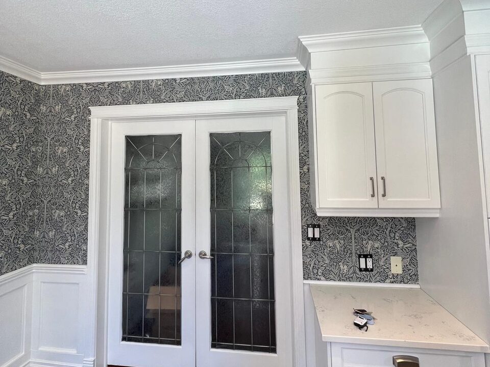 After photo of black and white botanical wallpaper installed around double doors and cabinetry in a Deer Run SE Calgary dining room