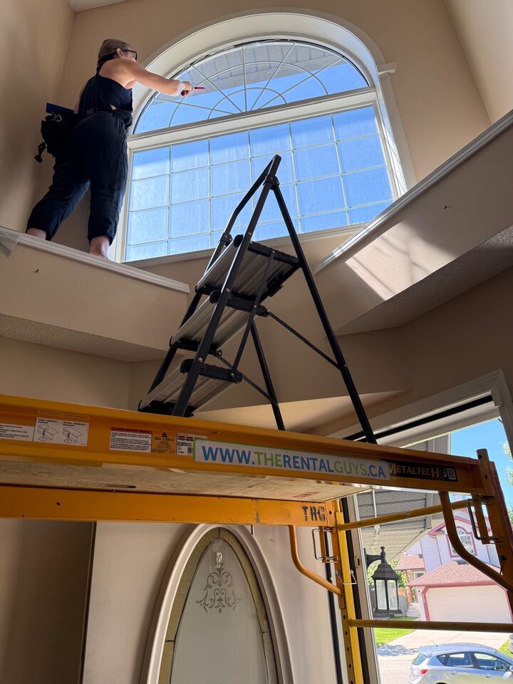 Installer on scaffold replacing solar window film on a two-storey arched foyer window in Douglasdale SE Calgary