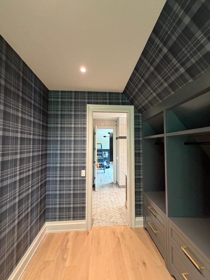Navy and charcoal tartan plaid wallpaper wrapped across the walls and sloped dormer ceiling of a walk-in closet in an Elbow Valley new build, Rocky View County