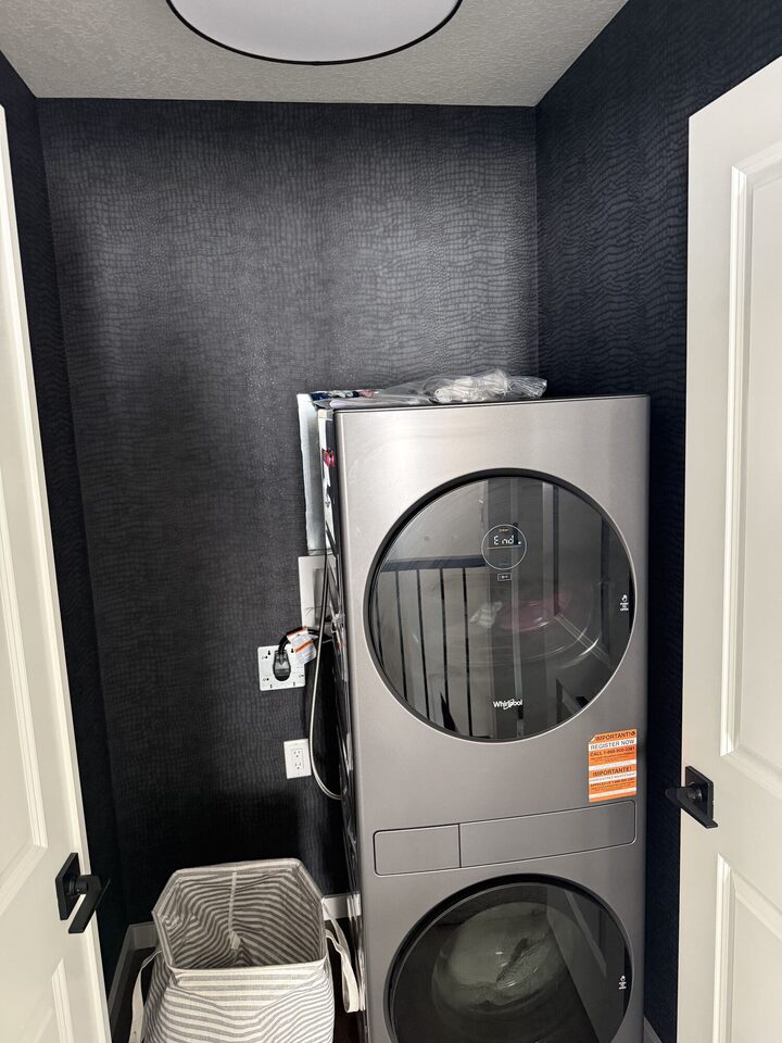 Crocodile-texture wallpaper wrapping a laundry room with a stacked Whirlpool washer and dryer, Heritage Hills, Cochrane