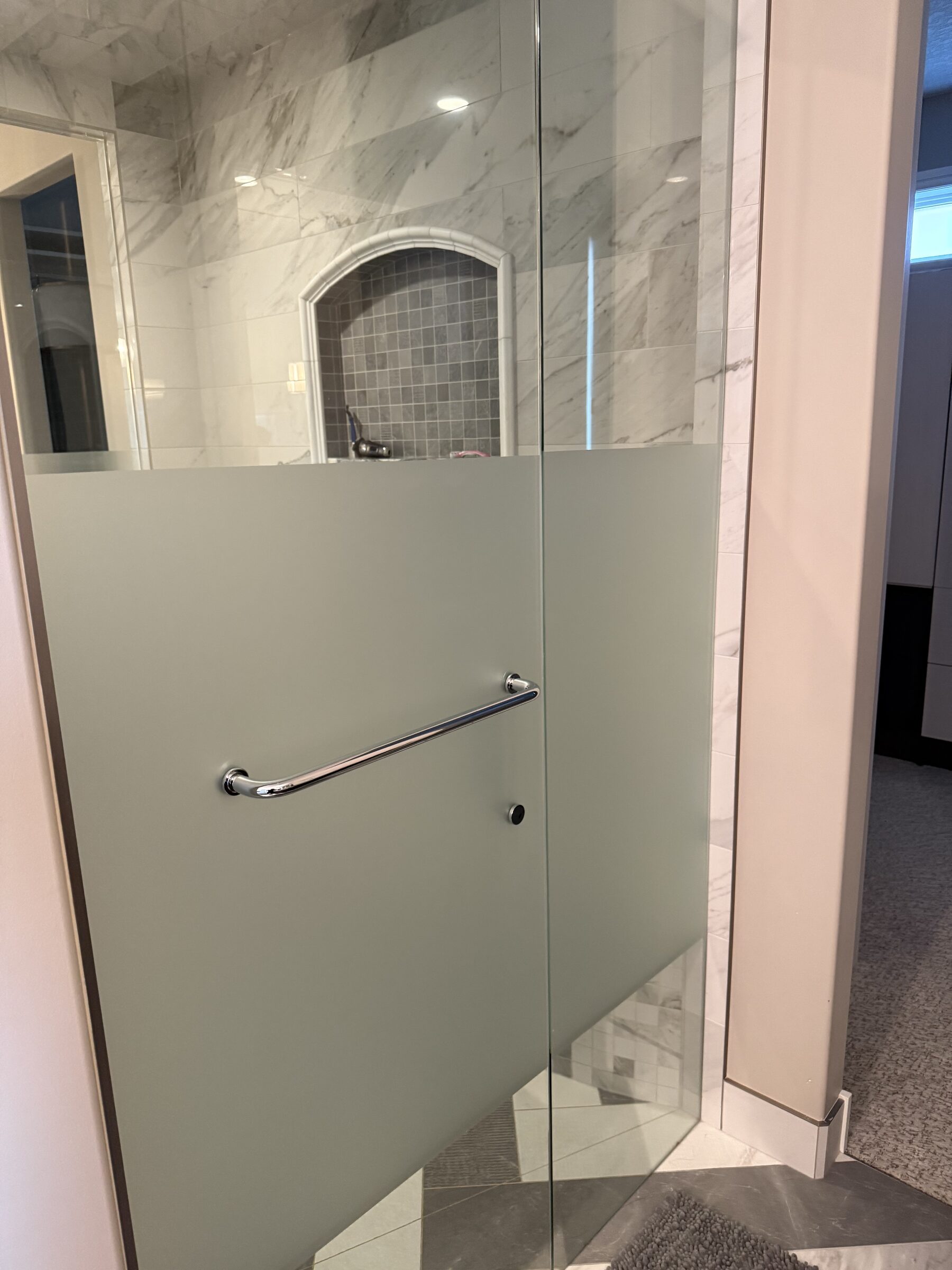 Finished shower enclosure with frosted privacy film band across the door and side panel in a marble ensuite in Heritage Pointe