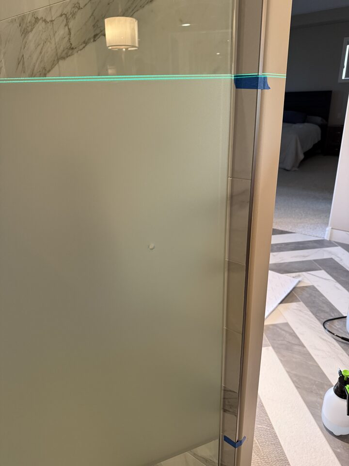 Frosted privacy film being applied to shower glass against a laser reference line in a Heritage Pointe ensuite