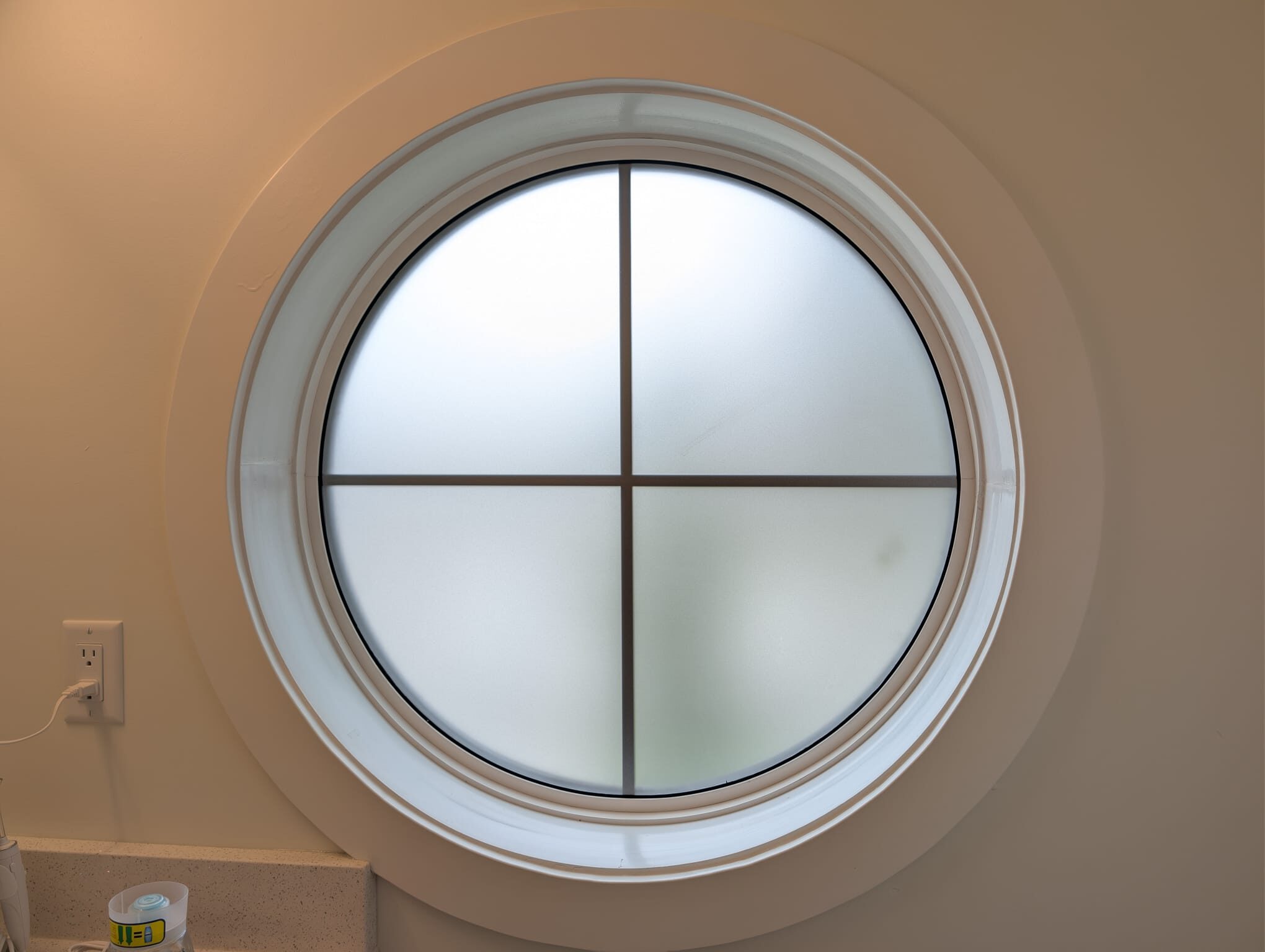 Round divided-lite bathroom window finished with frosted privacy film, glowing as a soft light panel, in a Highland Park NW Calgary home