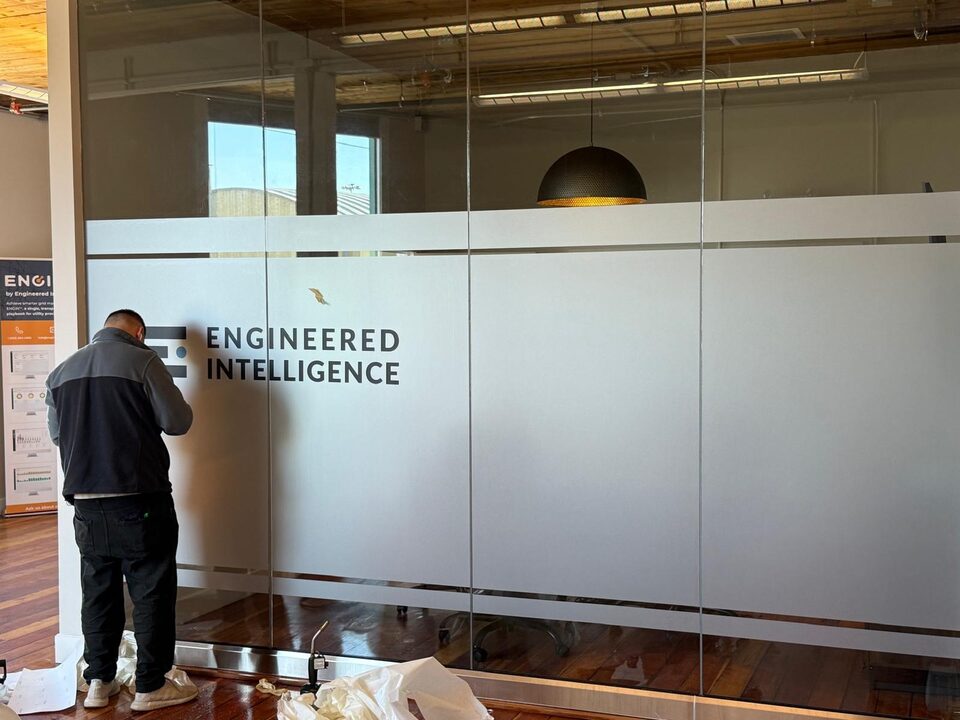 Install-progress photo of branded frosted privacy film being applied to office meeting room glass in Inglewood Calgary