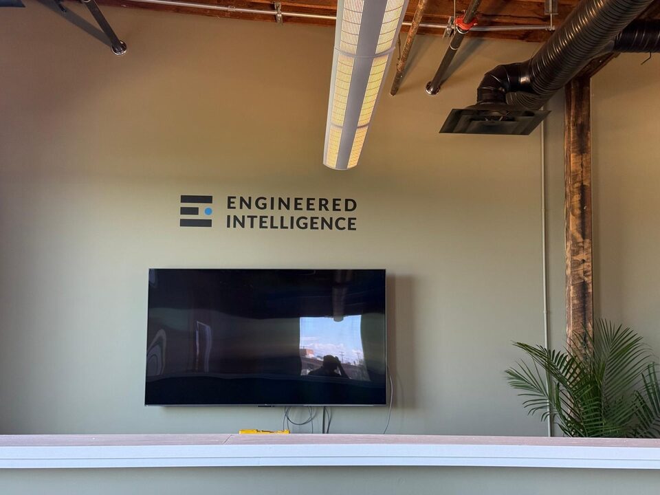 Finished custom company logo wall graphic installed above a mounted TV in an Inglewood Calgary office