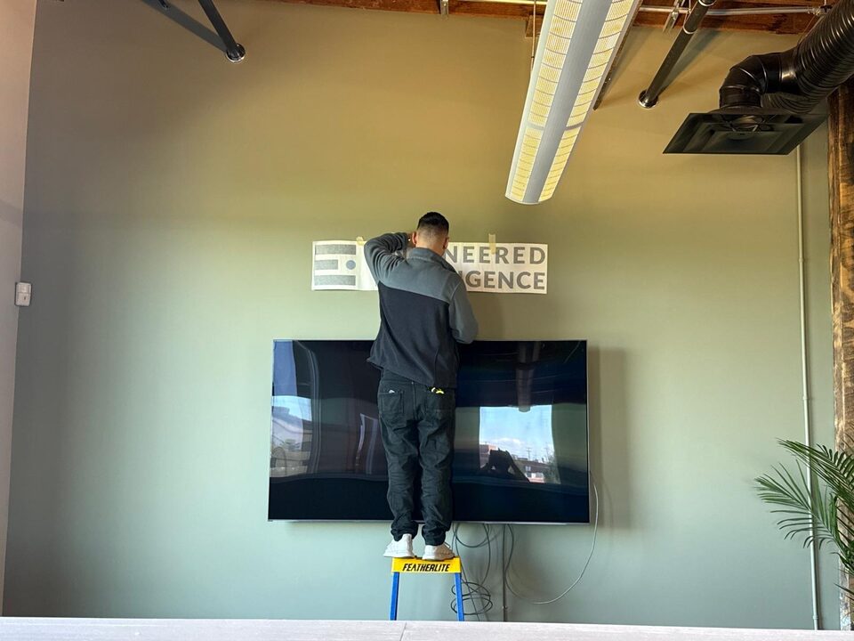 Alignment detail photo of a custom logo wall graphic being installed above a mounted TV in an Inglewood Calgary office