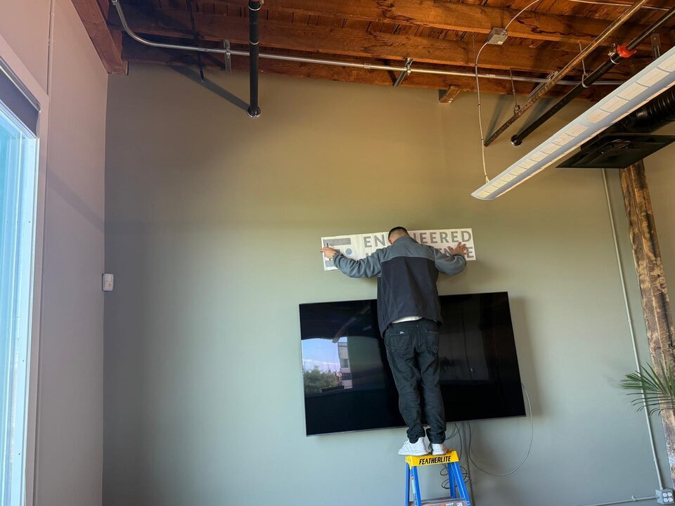Install-progress photo of a custom logo wall graphic above a mounted TV in an Inglewood Calgary office