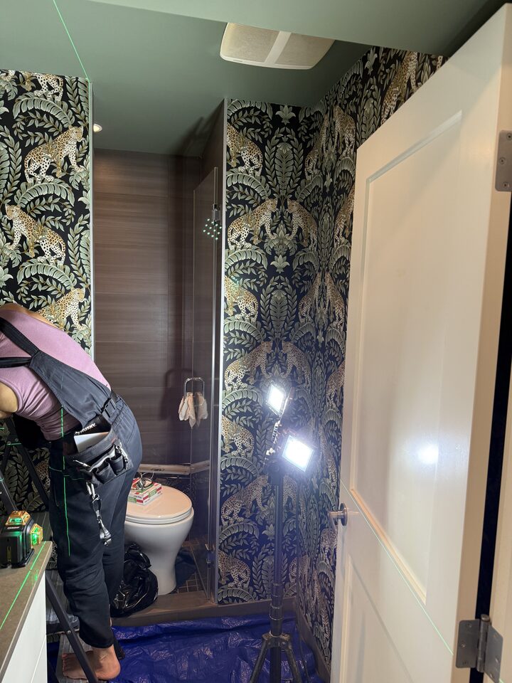 Installer trimming leopard print wallpaper above the shower during installation in a Parkland Calgary bathroom
