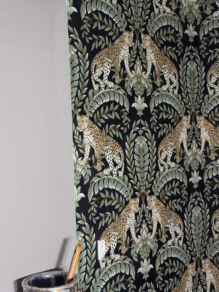 Pattern detail of mirrored leopards among sage ferns, wallpaper seam aligned across an outlet in a Calgary bathroom