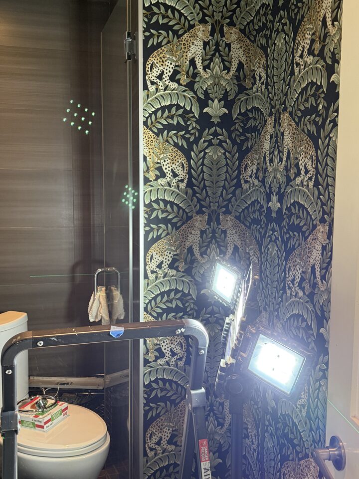 Laser-guided wallpaper installation in progress on the shower bulkhead wall of a SE Calgary bathroom