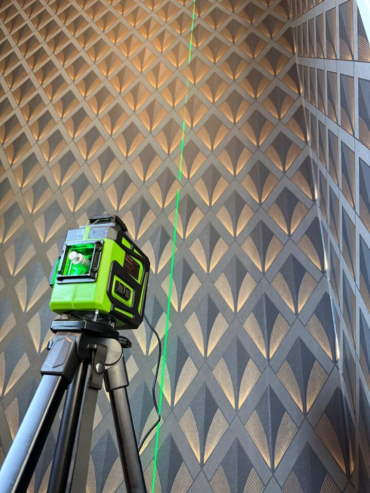 Laser level guiding art deco diamond wallpaper installation across a powder room corner in Patterson, SW Calgary