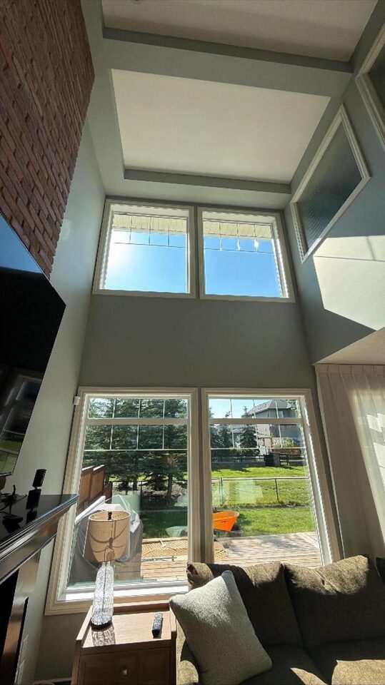 Bright two-storey living room with invisible solar window film on tall sky-facing windows in Silverado SW Calgary