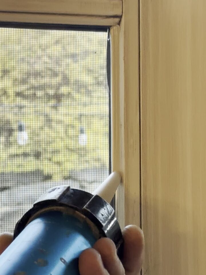 Installer running a sandstone DOWSIL 995 silicone bead along the glass-to-frame edge of a custom-painted French door to anchor security window film, Upper Mount Royal, Calgary