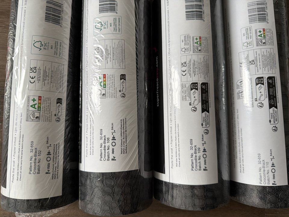 Four rolls of the same wallpaper pattern showing four different batch numbers on the manufacturer labels