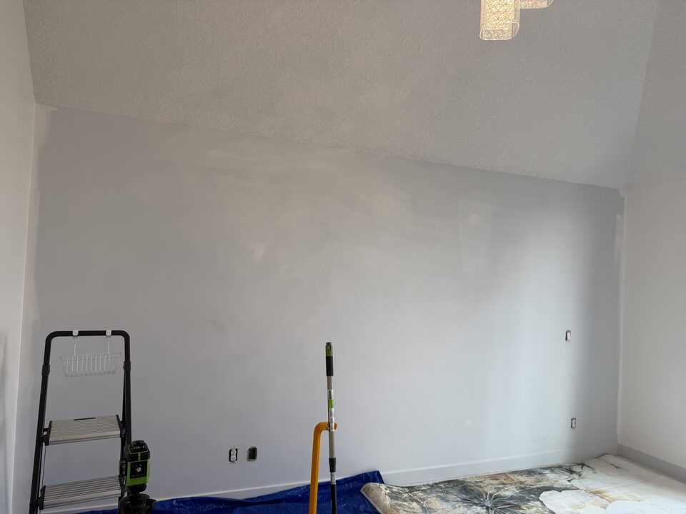 Primed bedroom feature wall with laser level and mural panels staged before wallpaper installation in Winston Heights, NE Calgary